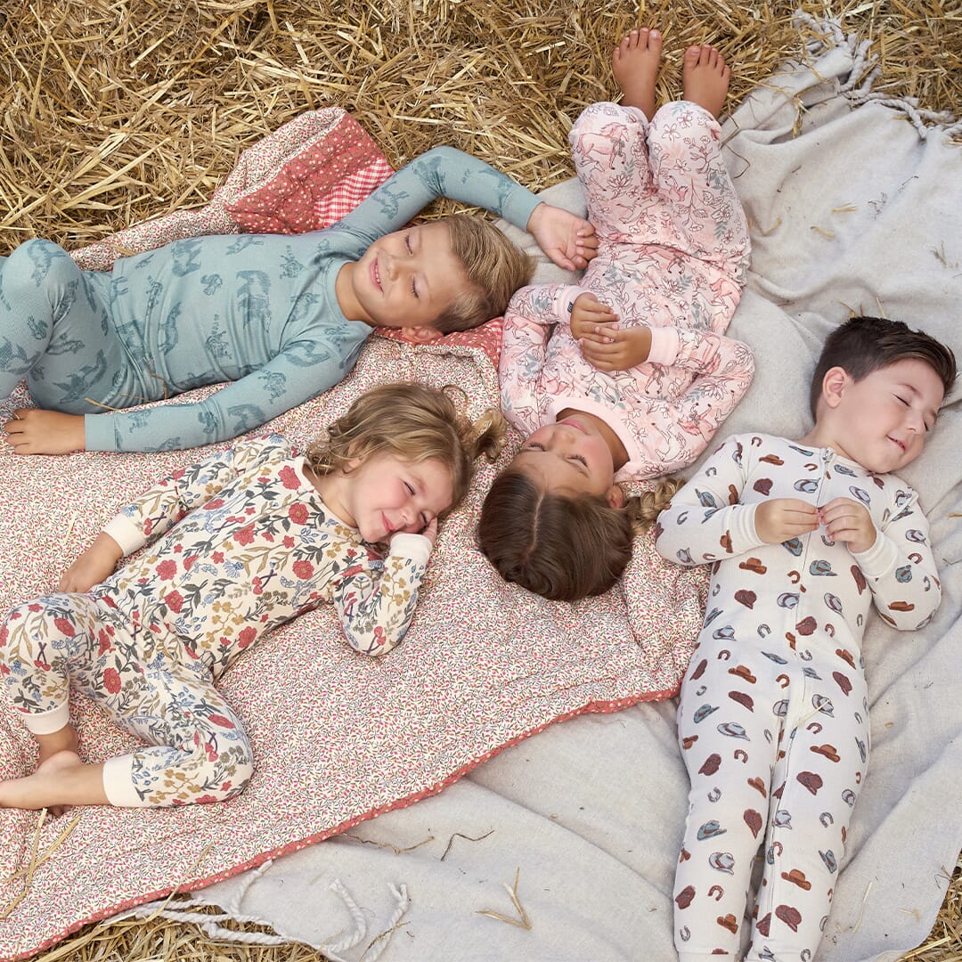 Children wearing patterned pajamas lying on a blanket outdoors.
