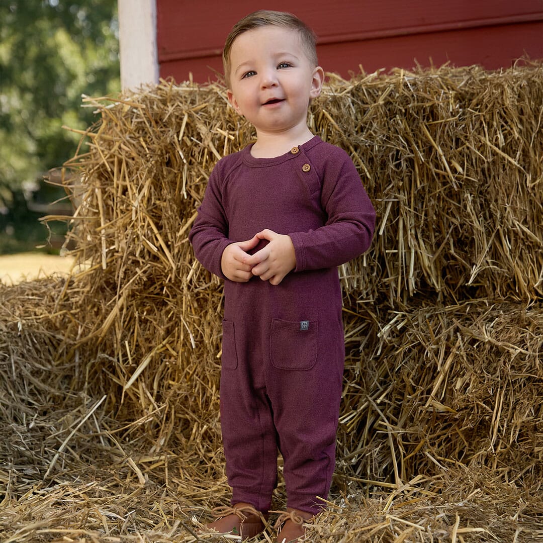 Child in a purple outfit standing on hay bales with a red barn in the background