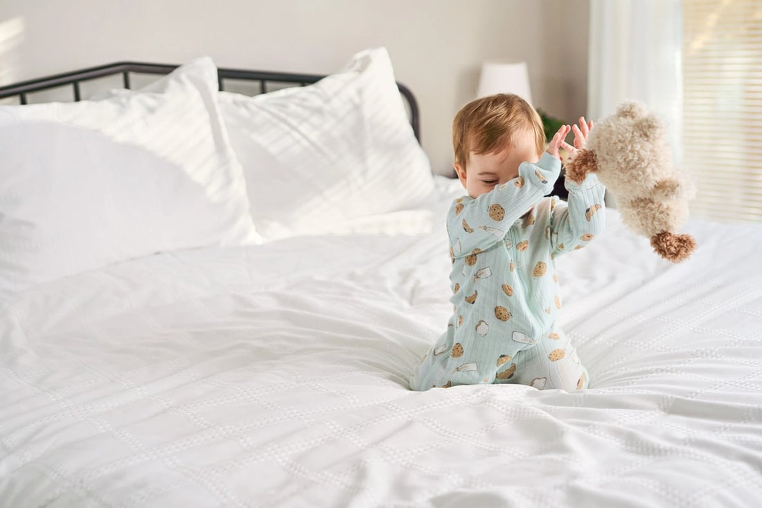 Child in pajamas sitting on a bed holding a plush toy