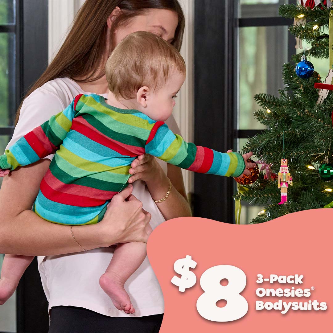 A baby wearing a colorful striped 3-pack onesie bodysuit is held by a woman in a home setting next to a decorated Christmas tree, with a pink promotional graphic overlay in the corner.