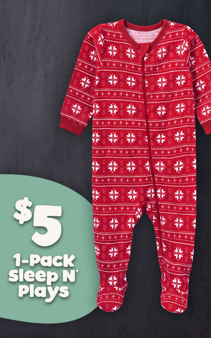 A red baby footed sleeper with a white holiday snowflake pattern, displayed on a dark gray background with a green promotional badge on the bottom left.