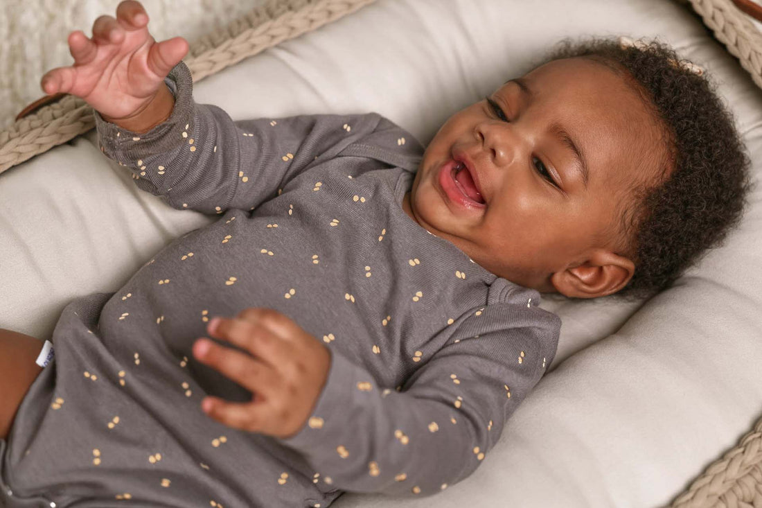 Baby lying on a cushion wearing a gray onesie with small patterns.