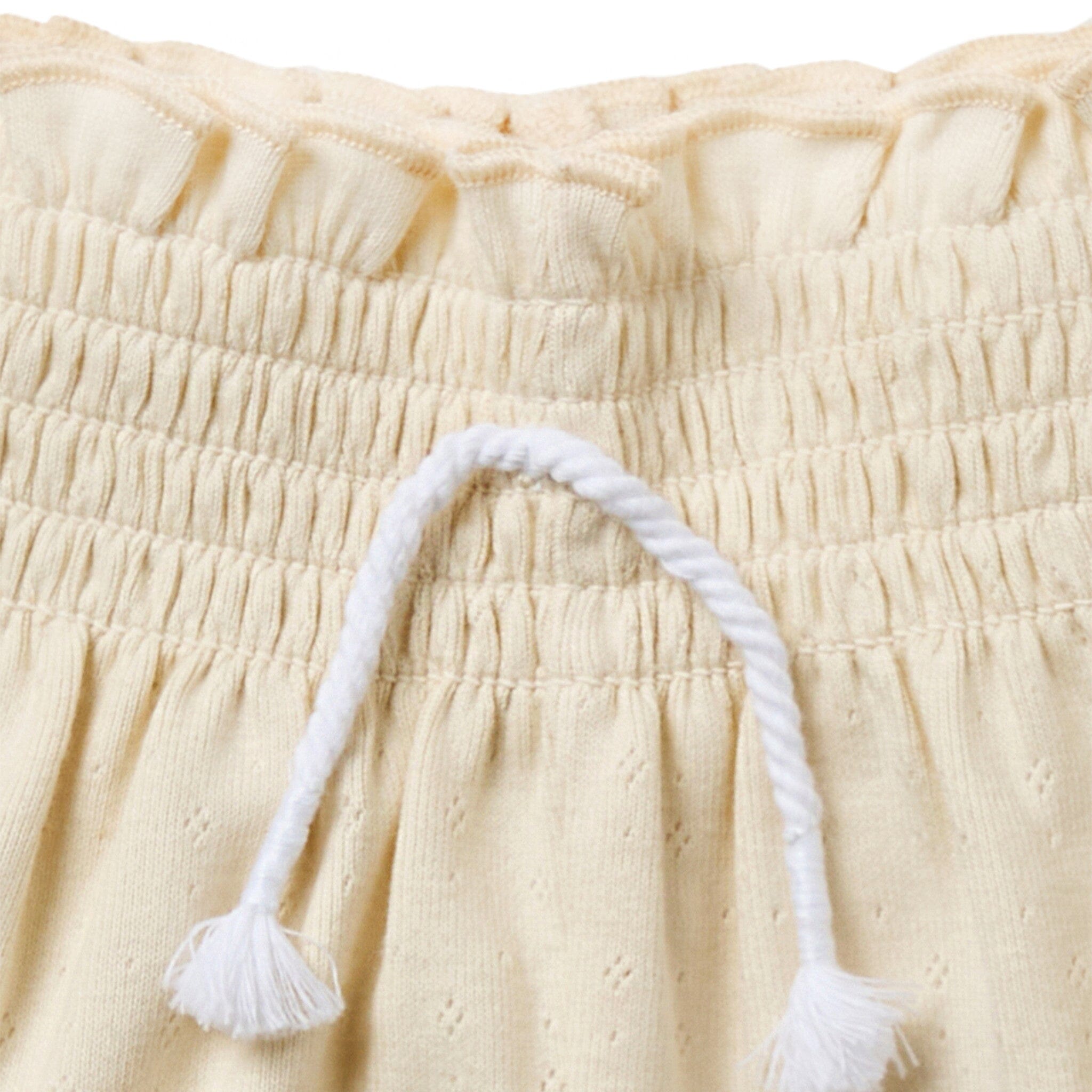 Close-up of beige fabric with a white tassel on a beige background