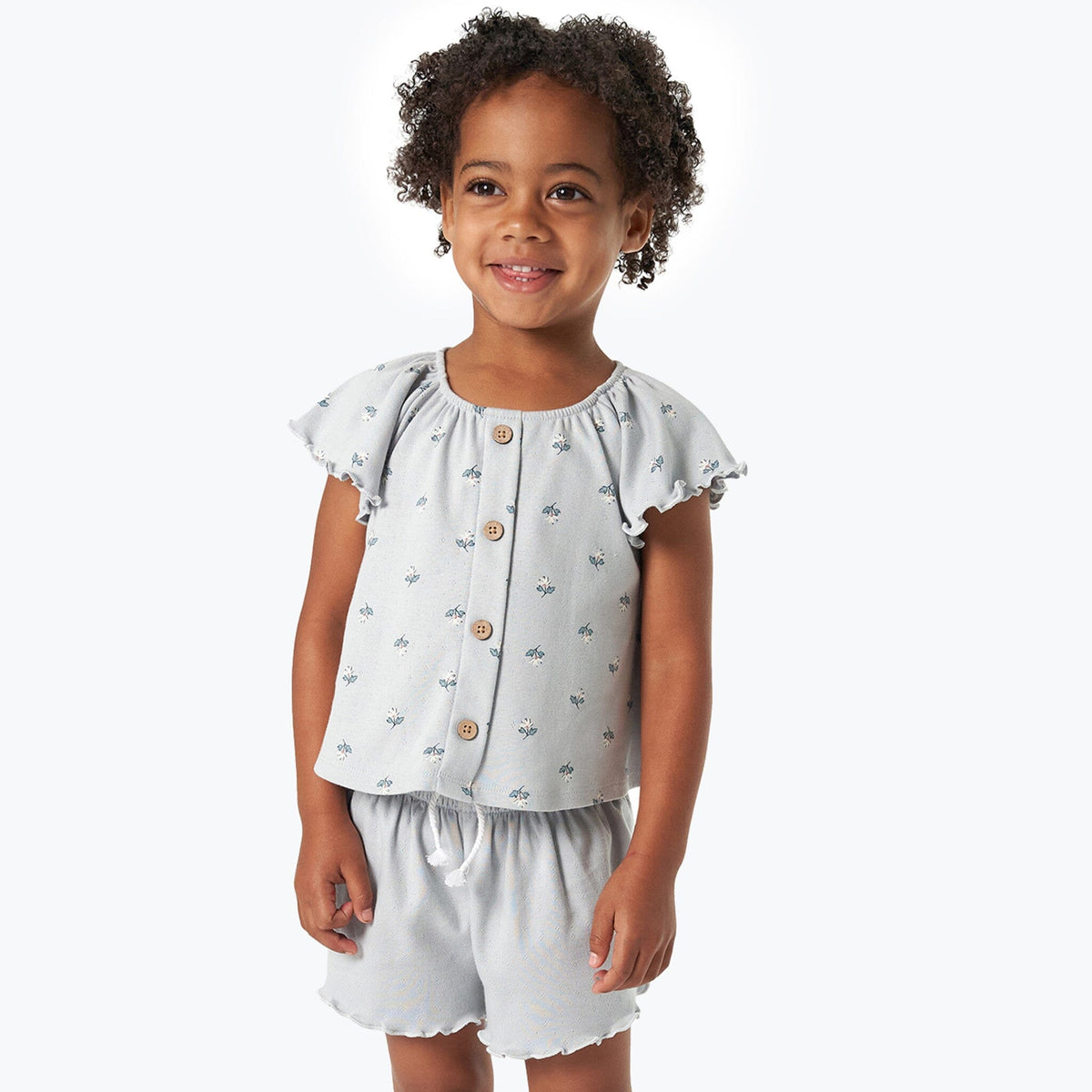 Young girl wearing a light blue floral top and shorts set on a white background