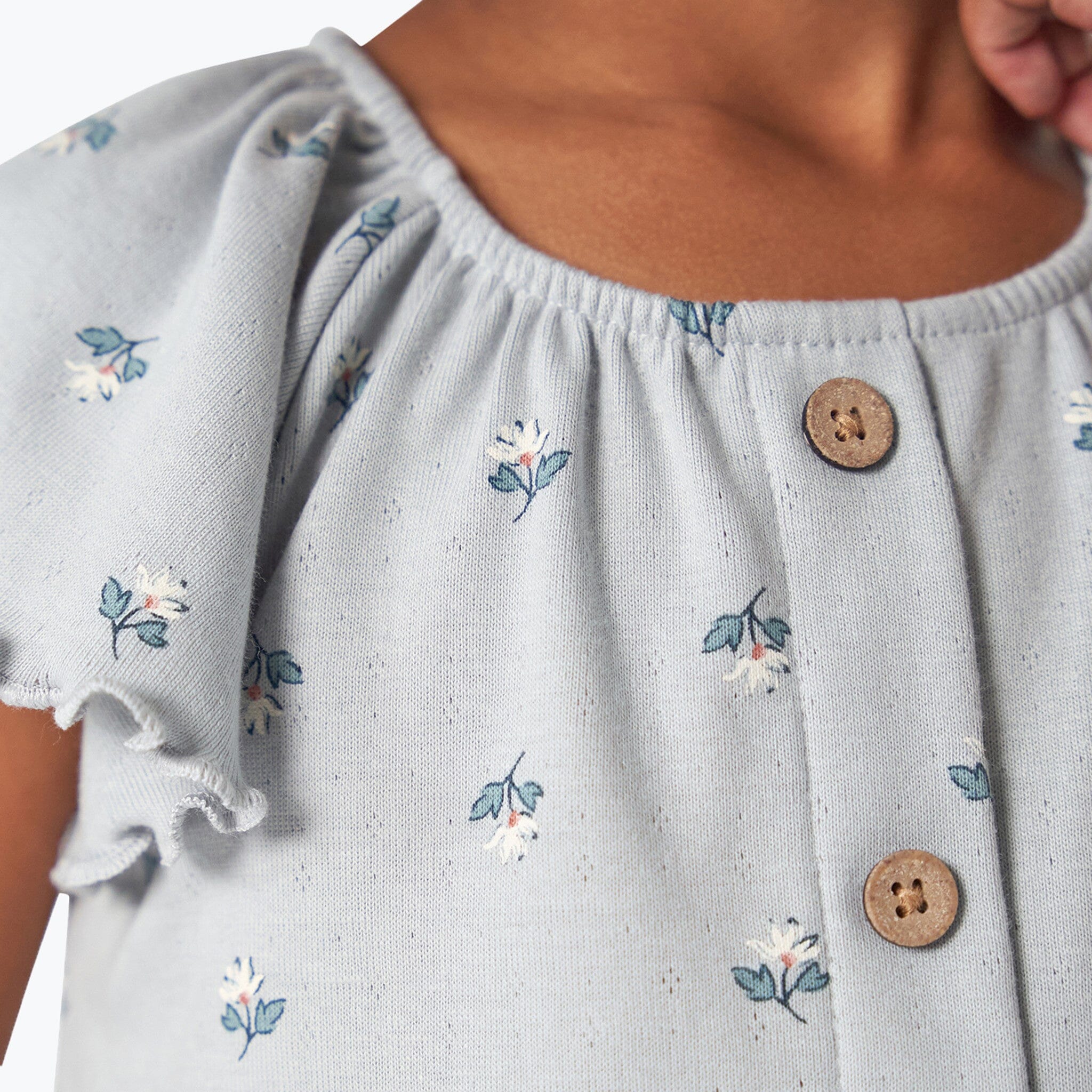 Light blue dress with floral embroidery and wooden buttons on a white background