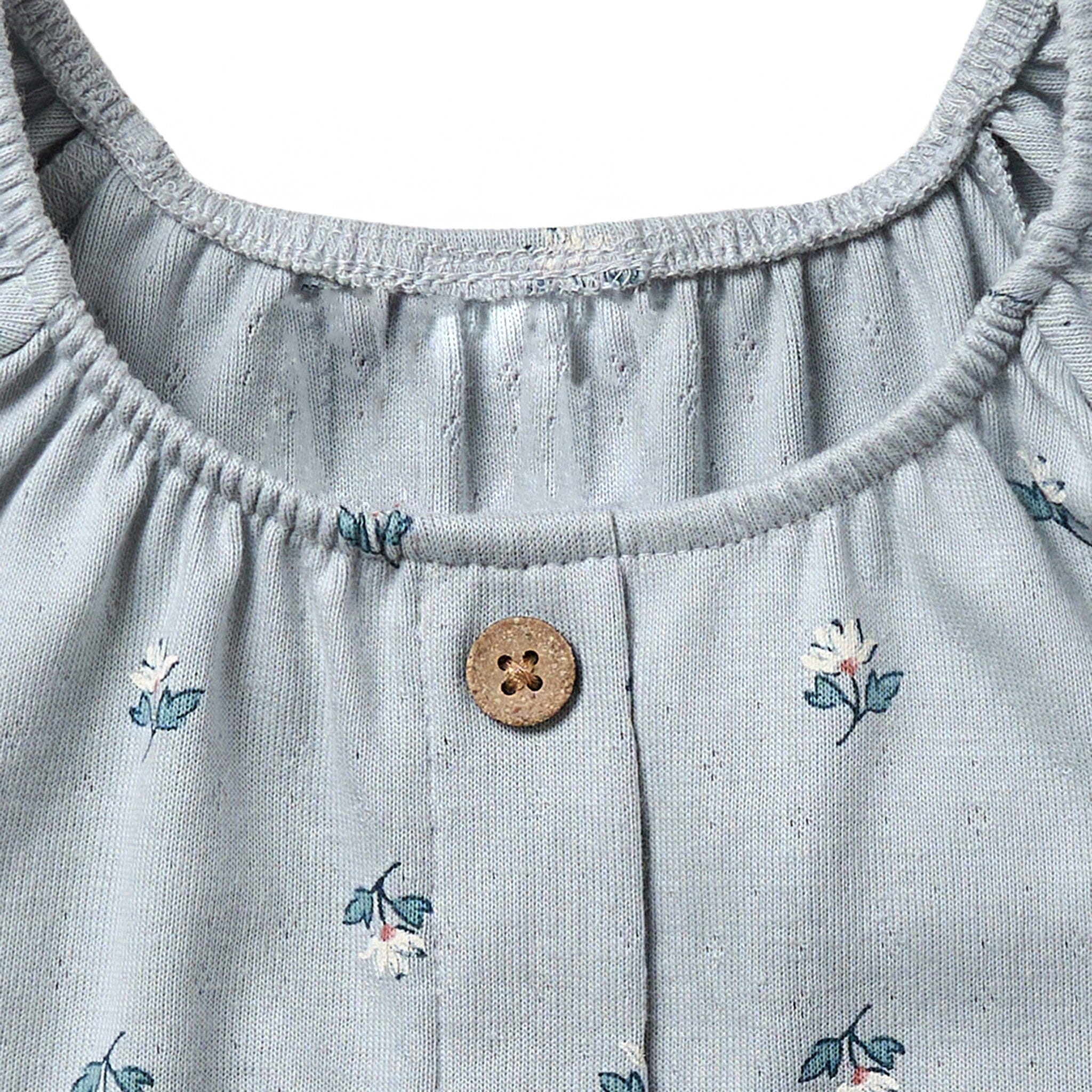 Close-up of a light blue dress with floral embroidery and a button detail.