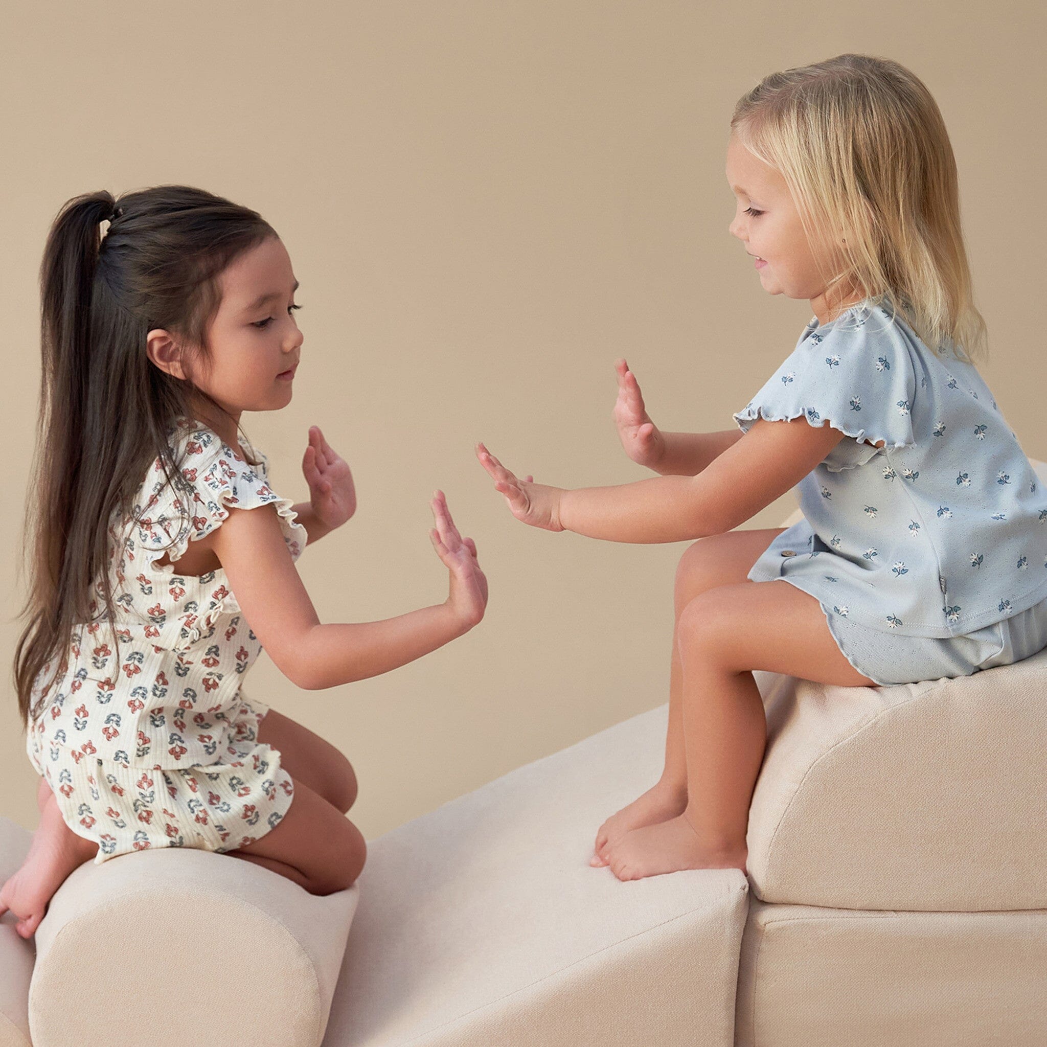 Two young girls playing with their hands on a beige couch.