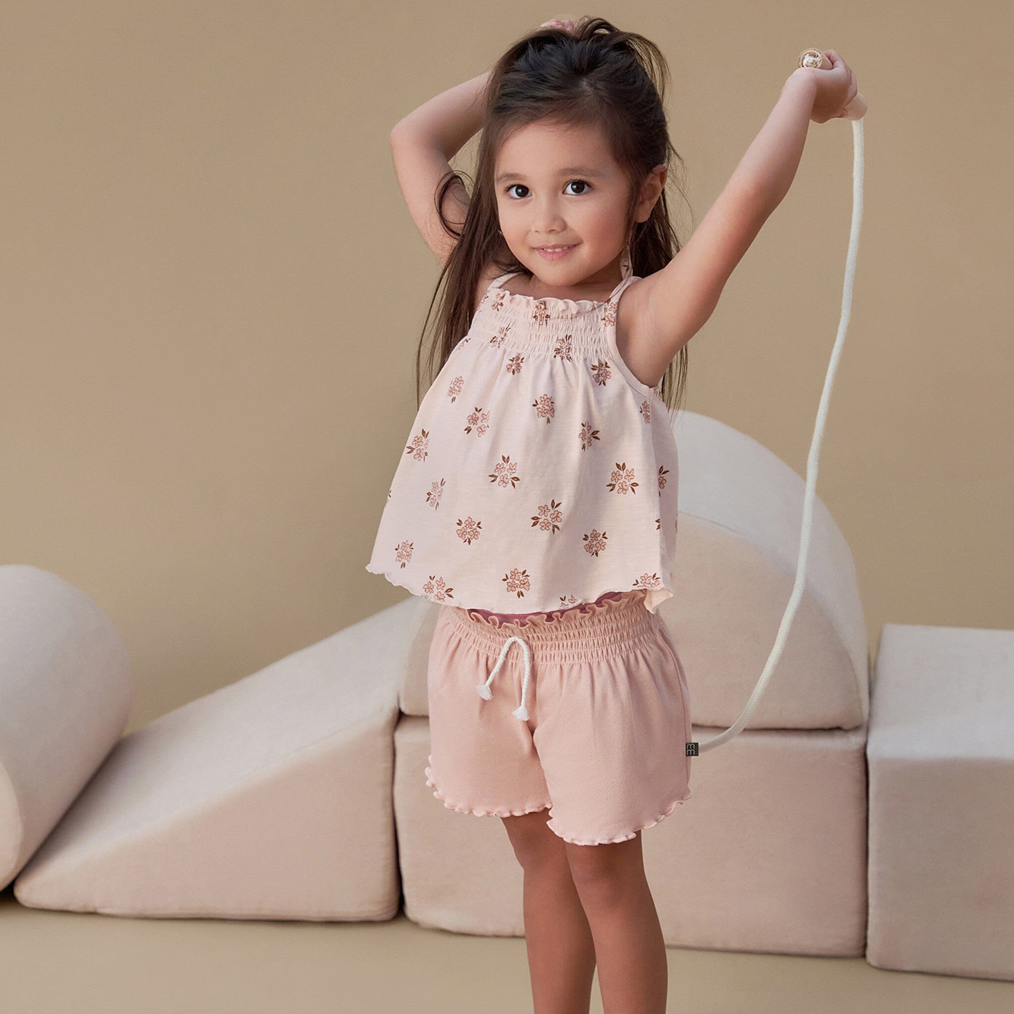 Young girl in a floral top and shorts standing in front of a beige couch.