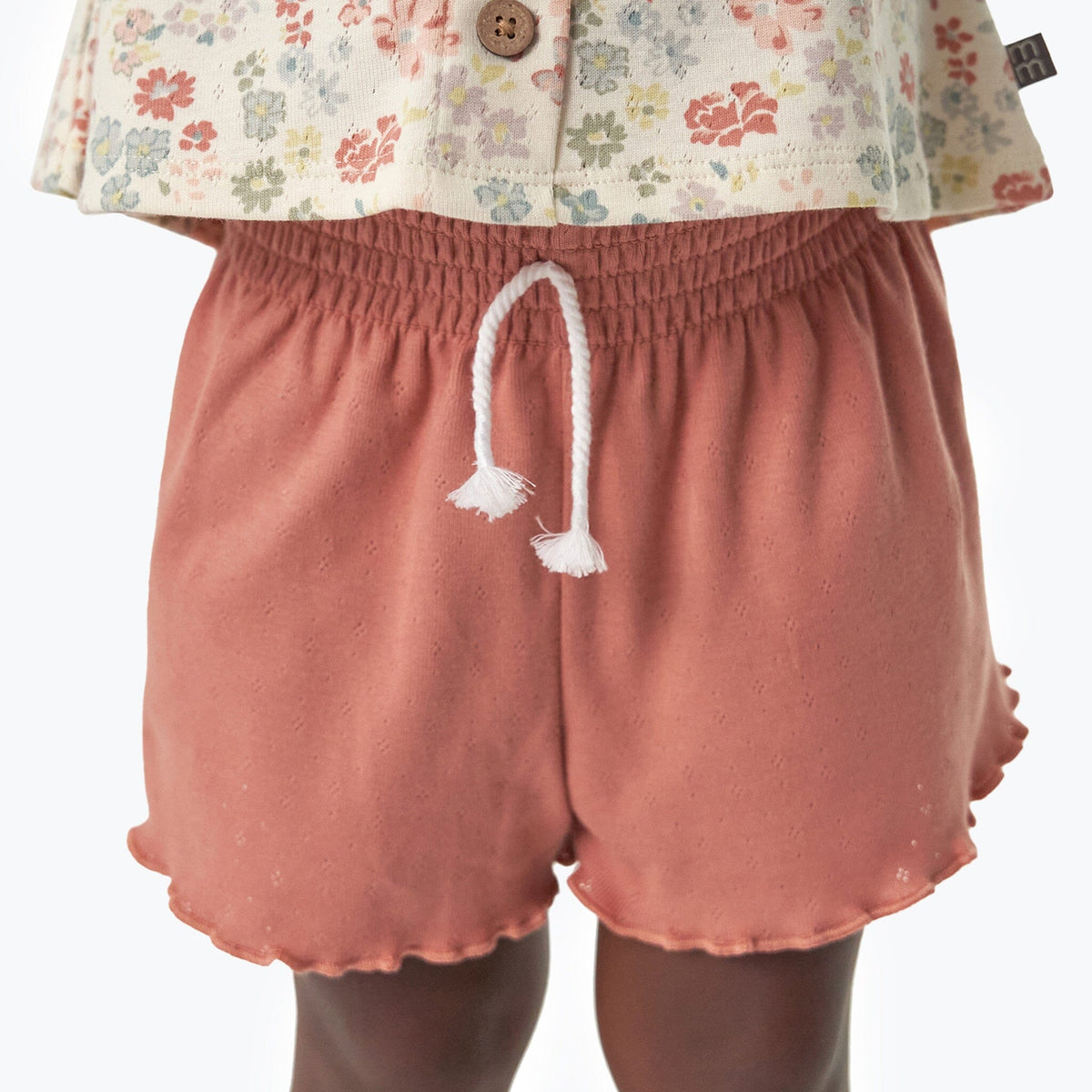 Pink shorts with a white button and drawstring on a white background